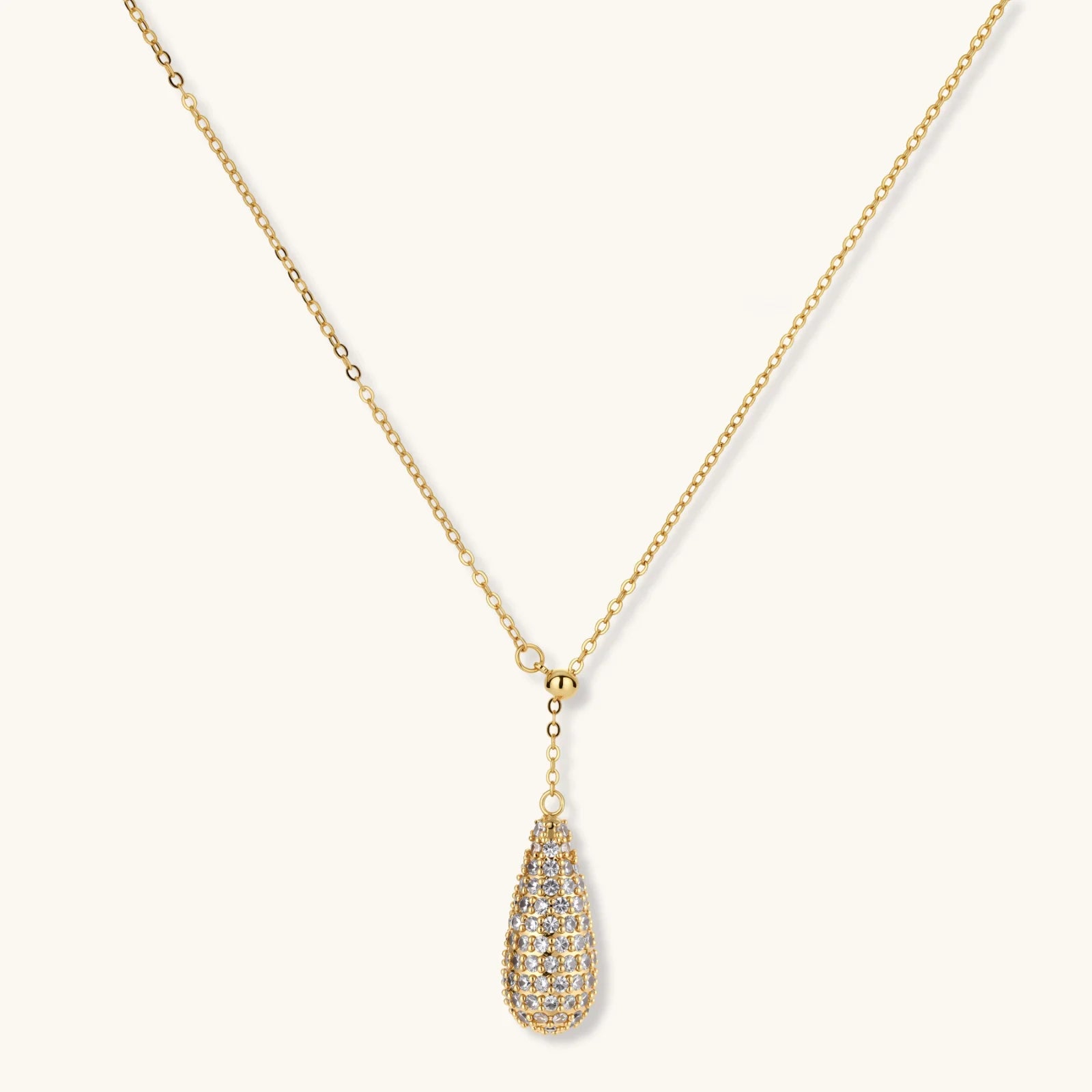 Gold-plated teardrop necklace and earrings covered in AAA cubic zirconia crystals on cream background.