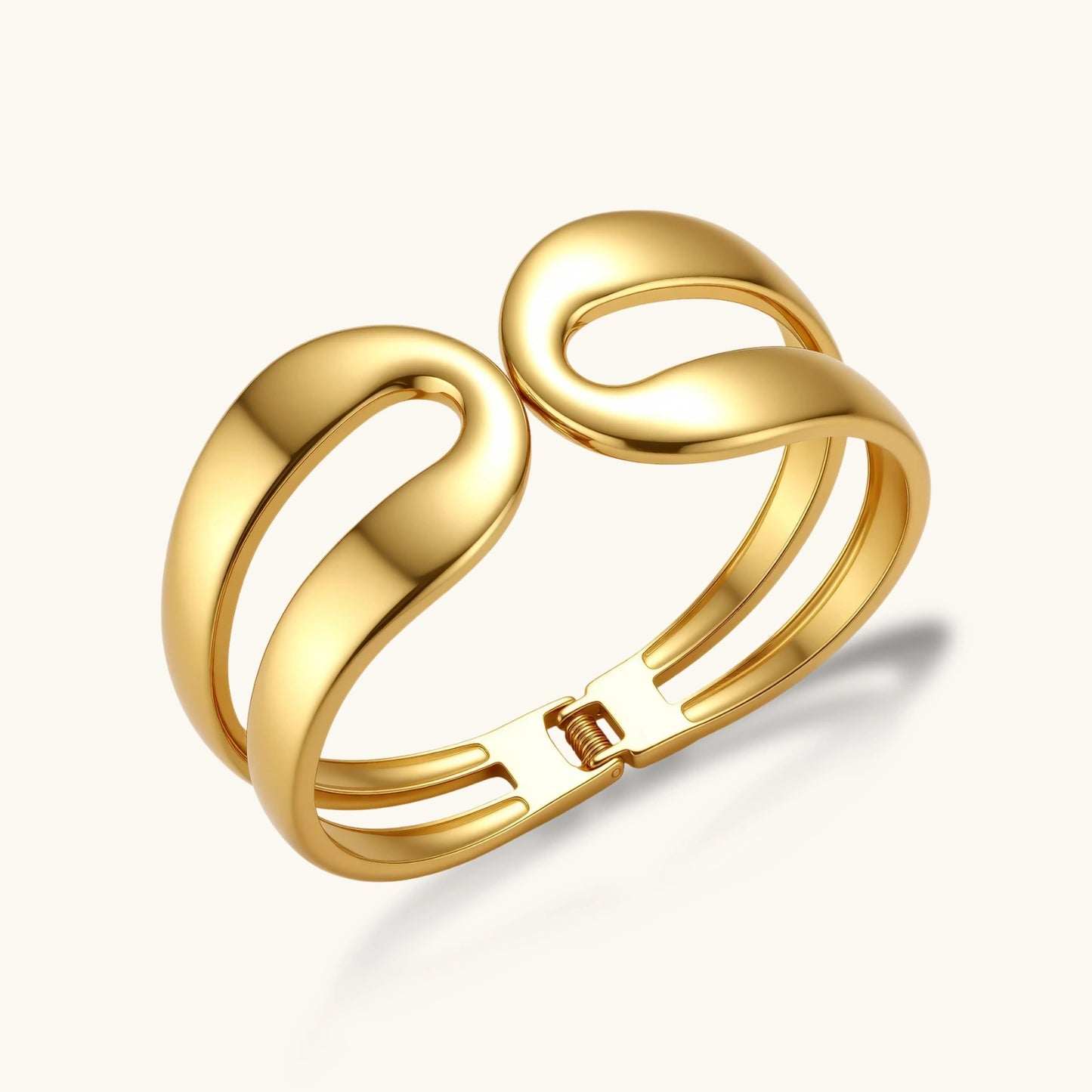 Polished 18K gold plated stainless steel cuff with two sculpted loops and a triple-band body with spring hinge clasp.